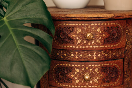Handmade wooden bedside table decorated with wood carvings and ornaments.The monstera leaf is close-up next to the pedestal.Creative background.Home interior design.