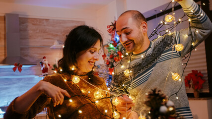 Man and woman tangled in garland of twinkle lights while decorating for christmas eve celebration....