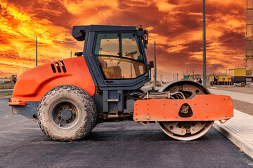 Heavy-duty vibratory roller for asphalt paving against the backdrop of a bright sunset sky. Road construction. Construction of roads and urban transport communications.