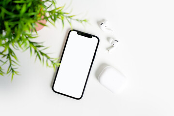 On the white table there is a smartphone with a white display and Bluetooth headphones.