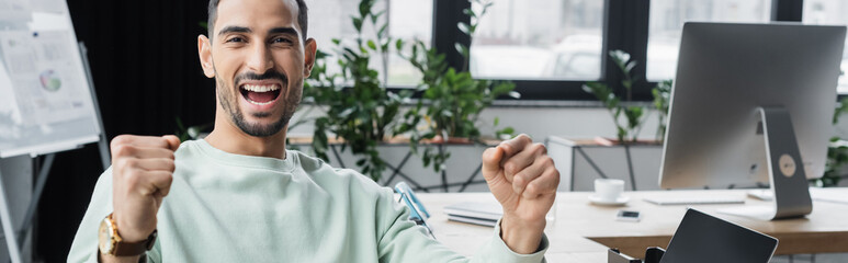 Excited arabian businessman showing yes gesture in office, banner