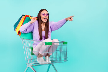Photo of excited lady sit cart carry bags ride finger empty space wear sunglass shirt isolated teal...