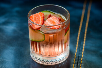 alcoholic cocktail with strawberries and cucumber on blue background with stitching close-up
