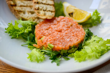 salmon tartare on a pillow with avacado served with lettuce lemon and toast close-up
