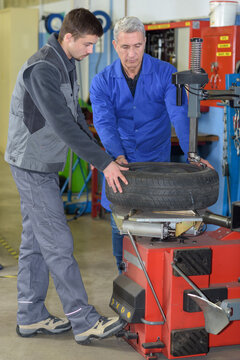 apprentice mechanic and teacher retreading wheel in automotive workshop