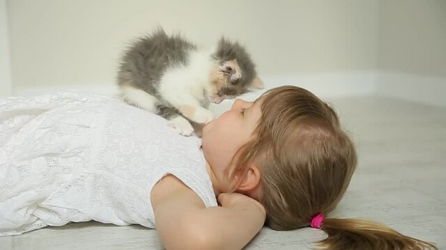 cute  funny little girl playing with a kitten on the floor lying on her back
