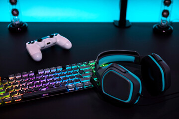 Various color backlighted gaming accessories on grey desk. Cyan illuminated wall.