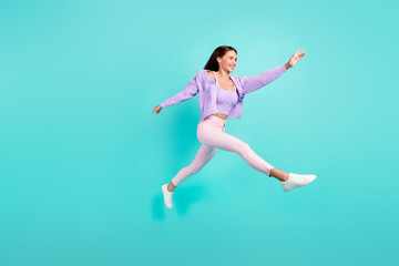 Fototapeta na wymiar Photo of pretty charming young woman dressed purple clothes running fast jumping high smiling isolated teal color background