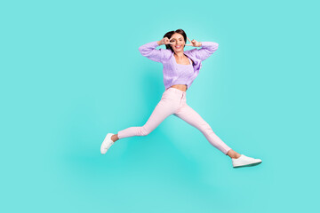 Photo of friendly lady jump show two v-signs wear violet cardigan trousers footwear isolated teal color background