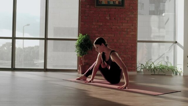 Young woman in red sports uniform trying to do Astavakrasana asana in yoga studio. Balance exercise. Straddle press handstand and Stretching on mat while practicing. High quality 4k footage
