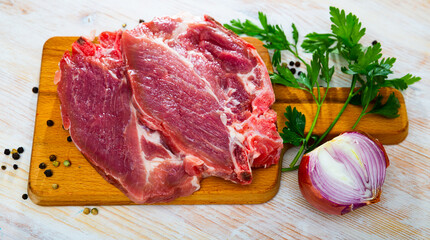 Raw pork chops served on wooden board with purple onion, parsley and black pepper