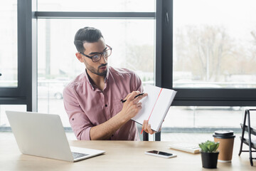 Fototapeta premium Arabian businessman pointing at notebook during video chat on laptop in office
