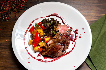 Chateaubriand of tender beef in Bordeaux wine sauce with vegetable sauté. Large plate of food on a dark brown wooden backdrop.
