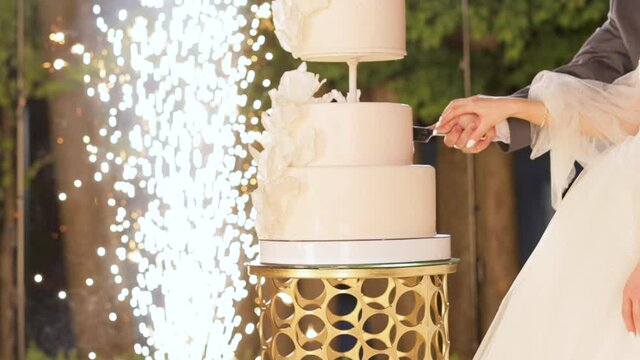 Wedding cake with sparklers in several tiers. Cut the wedding cake. The bride and groom cut the wedding cake. Detail of wedding cake cutting by newlyweds