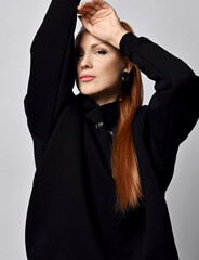 Portrait of gorgeous young woman vamp with healthy red hair in black sportswear holding arms up and...