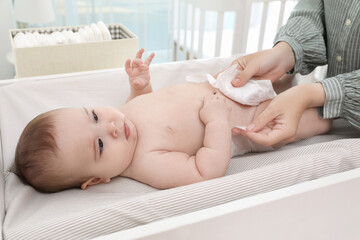 Mother changing baby's diaper on table at home