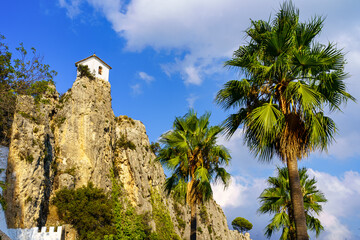 Fototapeta na wymiar Church on some rocks on a cliff next to large palm trees. Guadalest Alicante.