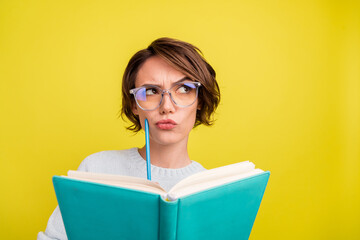 Photo of uncertain lady hold book pencil look empty space wear glasses blue sweater isolated yellow...