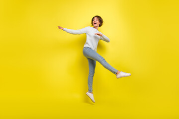 Fototapeta na wymiar Full size photo of impressed young brunette lady jump wear pullover jeans sneakers isolated on yellow background