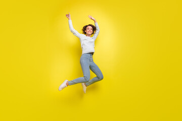 Fototapeta na wymiar Photo of carefree relaxed lady jump raise arms wear blue sweater jeans sneakers isolated yellow color background