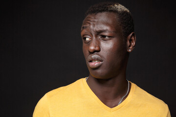 Close up of puzzled young african american man guy in yellow t-shirt posing isolated on black wall background studio portrait. People emotions lifestyle concept. Mock up copy space. Looking aside.