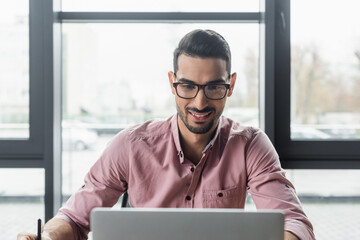 Smiling arabian businessman using blurred laptop in office