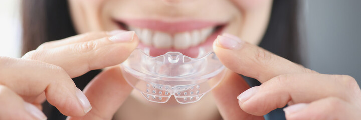 Smiling woman holds clear plastic mouthguard to straighten teeth