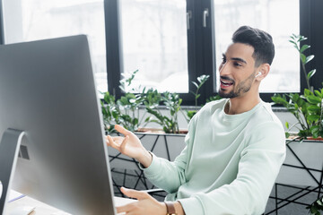 Positive muslim businessman in earphone having video call on computer in office