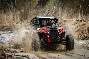 ATV/UTV/4x4 driving throw splashing past a muddy large puddle in forest