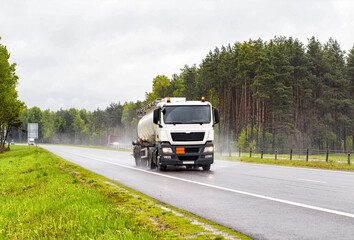 Fototapeta na wymiar A special vehicle for the transport of explosive substances travels along the road and transports oil products in rainy weather. Concept of the industry and transportation of petroleum products 