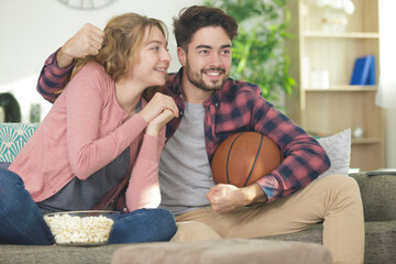 happy young couple watching basketball game on tv at home