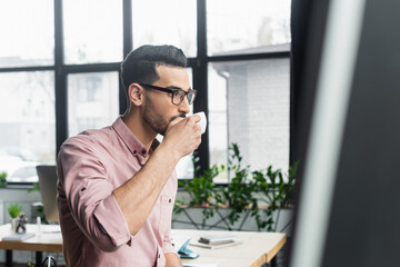 Fototapeta premium Arabian businessman in eyeglasses drinking coffee in office