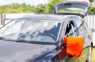An orange warning vest is hanging on the mirror of a passenger car. Car breakdown concept, roadside assistance signal