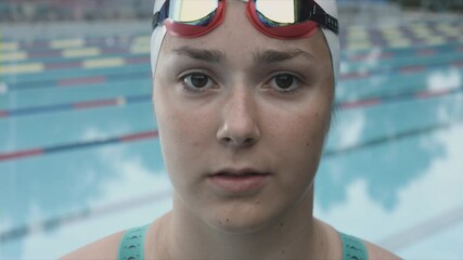 Close-up shot of a Caucasian girl, a sportswoman with a white swimming cap and goggles, looking at the camera.