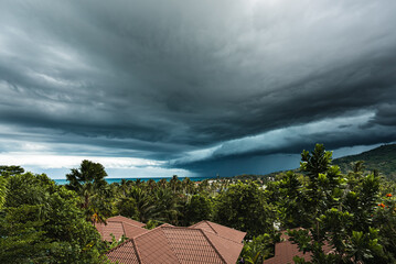 Dramatic storm clouds over the sea, forest and rooftops on a summer day