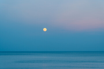 The full moon rises over the sea at a colorful sunset
