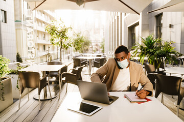 Young black man talking on cellphone while working with laptop at cafe