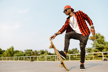 Young black man wearing plaid short skateboarding on parking