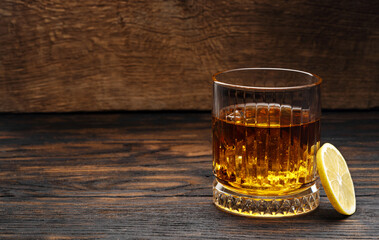 Whiskey or cognac or bourbon with ice on a wood background with lemon wedges