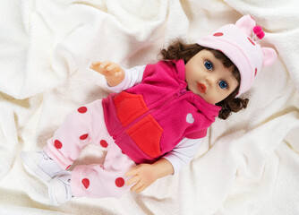 children's toy doll in a pink blouse lies on a white terry bedspread.