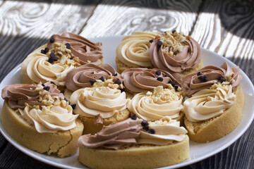 Sponge cake decorated with cream and chocolate drops.  Are laid out on a platter.  They stand on a surface made of pine boards.  Close-up shot.