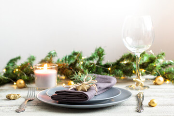 table setting for Christmas dinner with decorations on grey plate on white table. Holiday view with christmas tree.