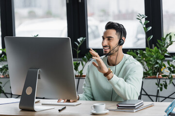 Positive muslim businessman in headset having video chat on computer in office