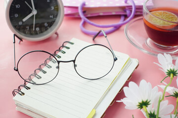Old eyeglass on a notepad on pink background 
