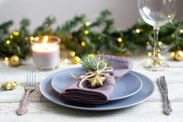 table setting for Christmas dinner with decorations on grey plate on white table. Holiday view with christmas tree.