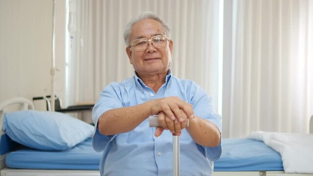 Portrait of smiling older Asian man sitting in wheelchair indoors. Happy senior retired disabled grandpa looking at camera relaxing at hospital
