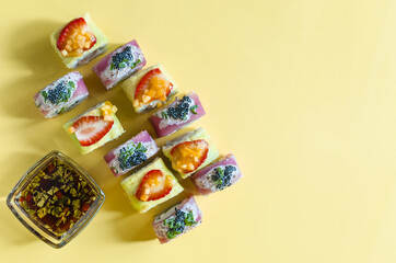 Bright rolls with seafood and fruit on a yellow background top view. Colored rolls, dark sauce and color background copy space