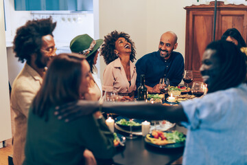 friends with good mood - people sitting around the table smiling and having fun - multiethnic diners at vegan party - women and men laughing happily