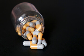 Pills on black background, bottle of medication in capsules. Concept of nutritional supplements, vitamins, antidepressants