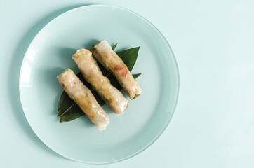 Spring rolls of seafood and vegetables in a light plate with a decor of green leaves on a light background.